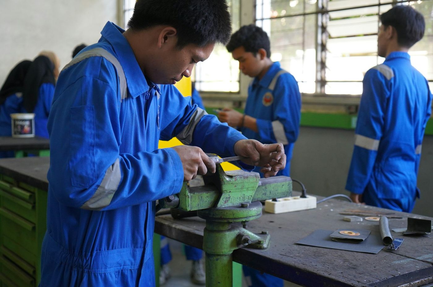 Young trainees in blue overalls practising at a workshop bench